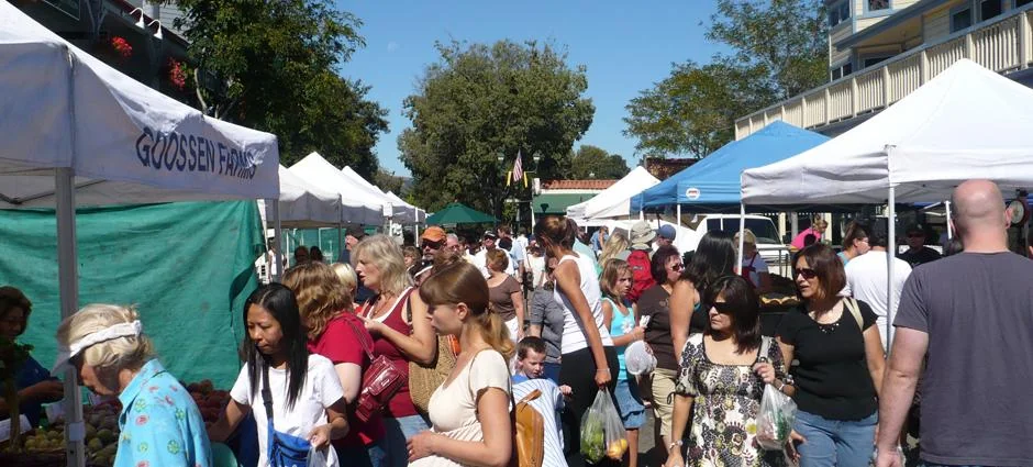 Pleasanton 农夫市集的白色帐篷、摊位与购物人群