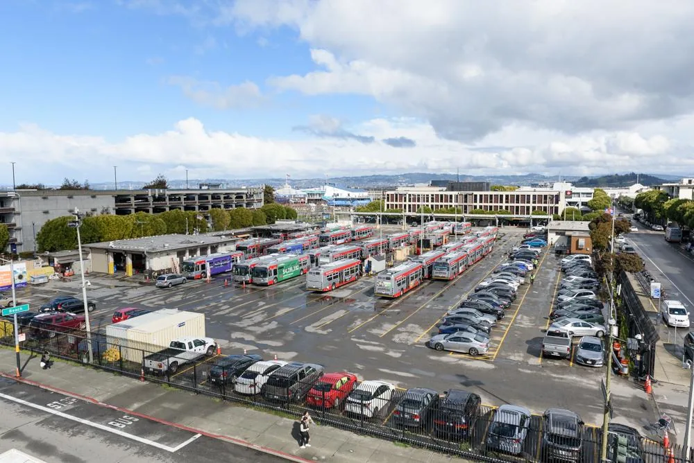 從高處看 Kirkland 公車場：停滿紅白色的 Muni 公車，四周停著私家車，旁邊人行道上有行人