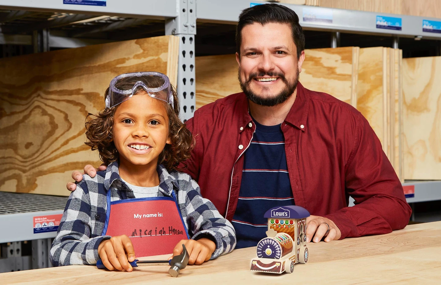 Lowe’s Holiday Engine 官方照片，儿童与成人在工作台展示节日火车头成品